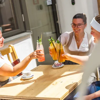 Benefits Three women in traditional clothing toasting with colorful summer drinks at a sunny outdoor table